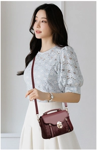 Detail of burgundy crossbody bag with snakeskin texture and metal clasp on model