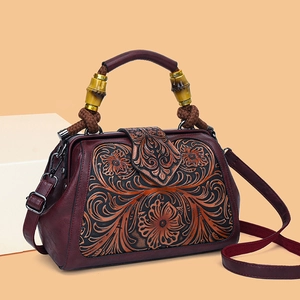 Retro red-brown leather handbag with floral embossing and bamboo handle on orange background