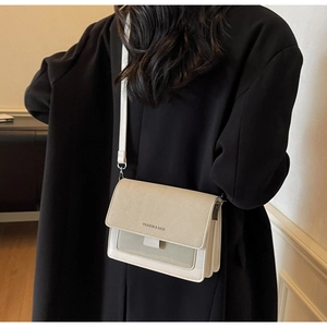 Dettaglio della borsa crema con logo Fashion & Bags su un cappotto nero alla moda