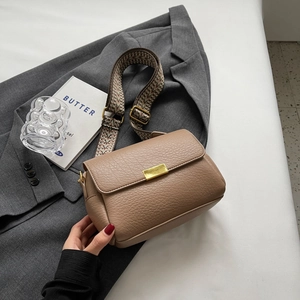 Brown litchi grain crossbody bag with wide geometric strap on grey blazer