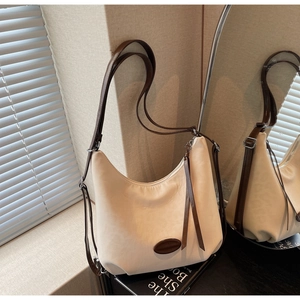 Detail view of a beige hobo bag with dark brown straps and sleek silver zipper closure