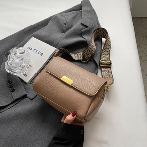 Brown lychee leather crossbody bag with wide jacquard strap on a grey suit jacket
