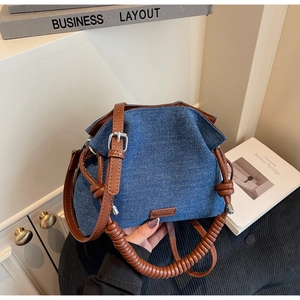 Close-up of denim bucket bag showing unique spiral handle and brown leather shoulder strap