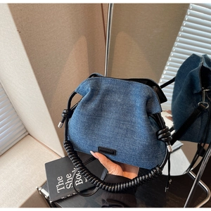 Detail of blue denim bucket bag featuring a thick black braided rope shoulder strap