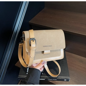 Dettaglio della borsa quadrata kaki con testo Fashion & Bags su sfondo di libri di lusso