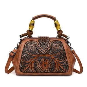 Retro brown leather handbag with embossed floral patterns and a bamboo handle on white back