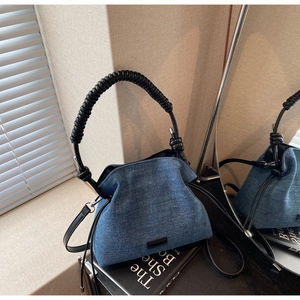 Close-up of blue denim bucket bag featuring a unique black spiral handle and slim leather strap