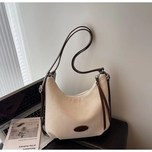 Detail of beige crescent shoulder bag next to a laptop showing textured fabric and leather strap
