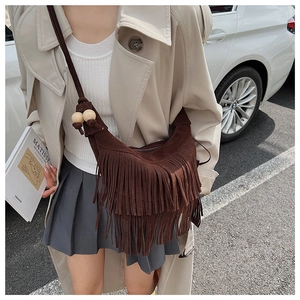 Detailed view of bohemian fringe crossbody bag with wooden beads in natural outdoor setting