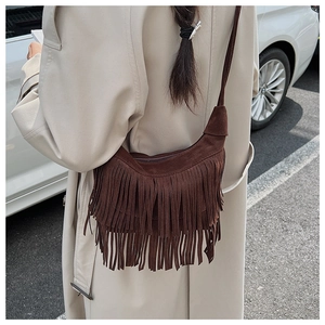 Detailed view of vintage brown suede tassel crossbody bag worn over a light trench coat