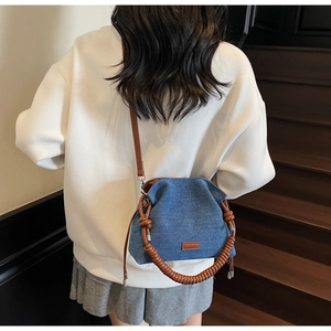 Blue denim cloud bag with brown woven strap and silver hardware on a wooden staircase