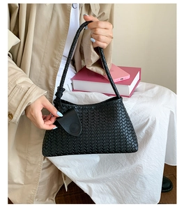 Close-up of black woven hobo handbag featuring a knotted handle and leather pendant detail
