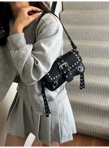 Close-up of black punk shoulder bag with silver studs and decorative buckles worn by model