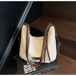 Detail of cream hobo bag with brown tassels and leather trim on a wooden background