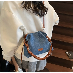 Detail of denim bucket bag with brown woven handle and leather strap on wooden stairs