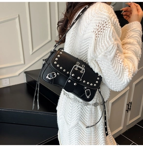 Close-up of black leather crossbody bag featuring punk silver rivets and large buckle detail