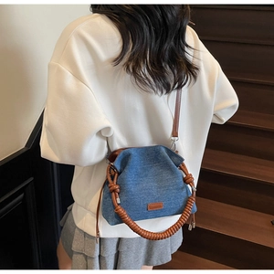 Close-up of blue denim crossbody bag with brown braided handle on model's back