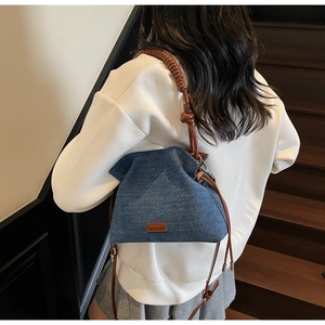 Detail of denim bucket bag showing brown leather patchwork and unique twisted shoulder strap