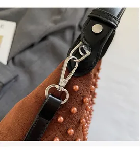 Detailed close-up of brown suede bag with pearl studs and silver metal hardware hook