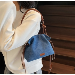 Detail of blue denim bucket bag with brown woven rope handle on a model