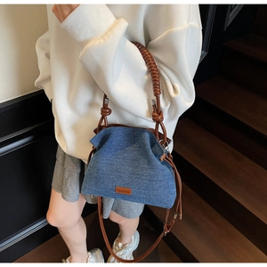 Detail of blue denim bucket bag featuring woven handle and adjustable brown shoulder strap
