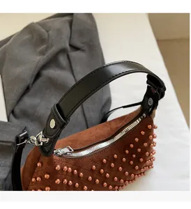Close-up of brown suede shoulder bag with bronze bead accents and black leather handle