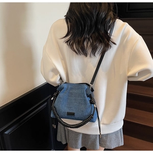 Blue denim cloud bag with black spiral handle shown on model's shoulder against stairs