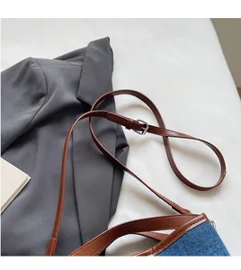 Detail of adjustable leather strap and denim patchwork on a stylish crossbody bucket bag