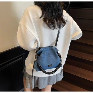 Detail view of a blue denim drawstring bucket bag with textured handle and shoulder strap