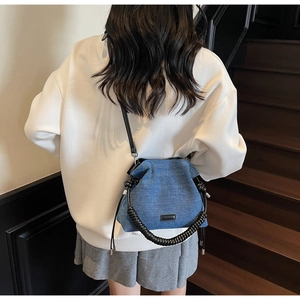 Detail of blue denim bucket bag featuring a spiral woven leather handle and minimalist tag
