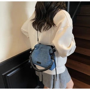 Detail of blue denim bucket bag with unique black spiral handle and drawstring closure