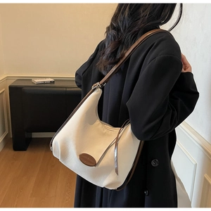 Detail of white canvas hobo bag with brown leather trim and adjustable metal buckles