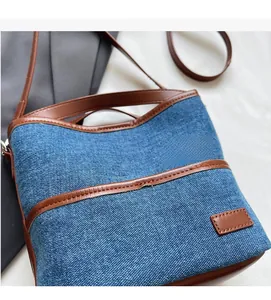 Detail of blue denim shoulder bag featuring brown leather trim and decorative patch pocket