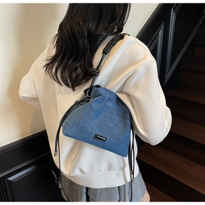 Detail of blue denim bucket bag with unique black spiral shoulder strap and drawstring