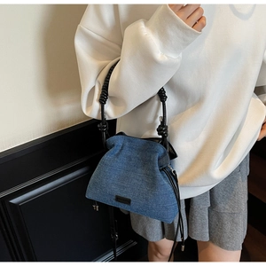 Detailed view of dark denim pleated cloud bag with black braided rope handles on model