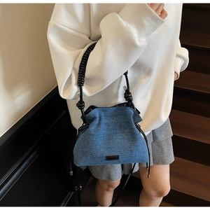 Detailed view of blue denim cloud bag with ruched texture and black spiral handles