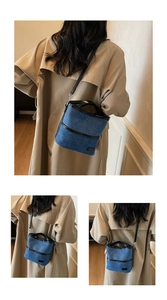 Blaue Denim Beuteltasche mit schwarzem Ledergriff und verstellbarem Riemen am Trenchcoat