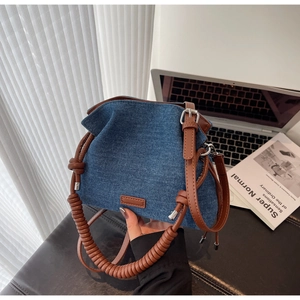 Detail of blue denim bucket bag with brown spiral handle and leather shoulder strap