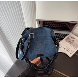 Close-up of denim shoulder bag with spiral handle and leather trim details