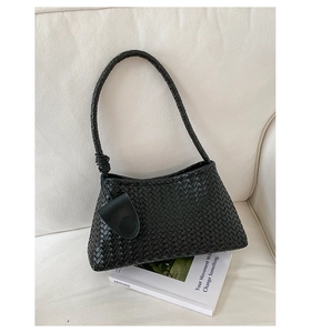 Close-up of black woven shoulder bag featuring side knot detail and small leather charm