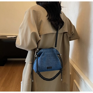 Detail of blue denim cloud bag with black spiral handle and textured pleats