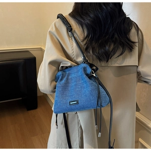 Detailed side view of blue denim cloud bag with black spiral strap and soft pleated texture