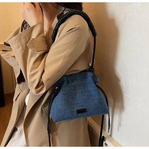Detail of blue denim hobo bag with spiral textured handle and drawstring on beige coat