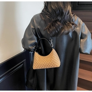 Detail of tan suede shoulder bag with gold studs on a model wearing a black coat