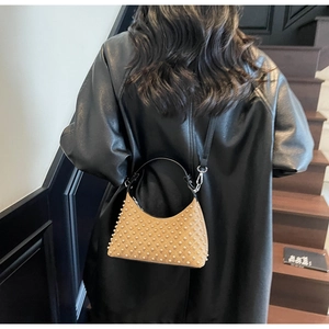 Detail shot of a brown studded crescent handbag styled on a model in a minimalist setting