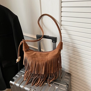 Brown faux suede fringe shoulder bag with wooden beads decoration on travel suitcase
