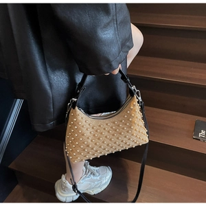 Detail of light brown punk style pearl shoulder bag with studded faux pearls and black handle