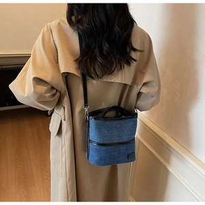 Detail of dark blue denim bucket bag with black leather piping and adjustable strap