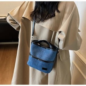 Close-up of denim bucket bag with black leather trim worn with a khaki trench coat