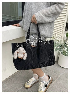 Close-up of black pleated leather tote bag featuring a cute white plush bunny charm